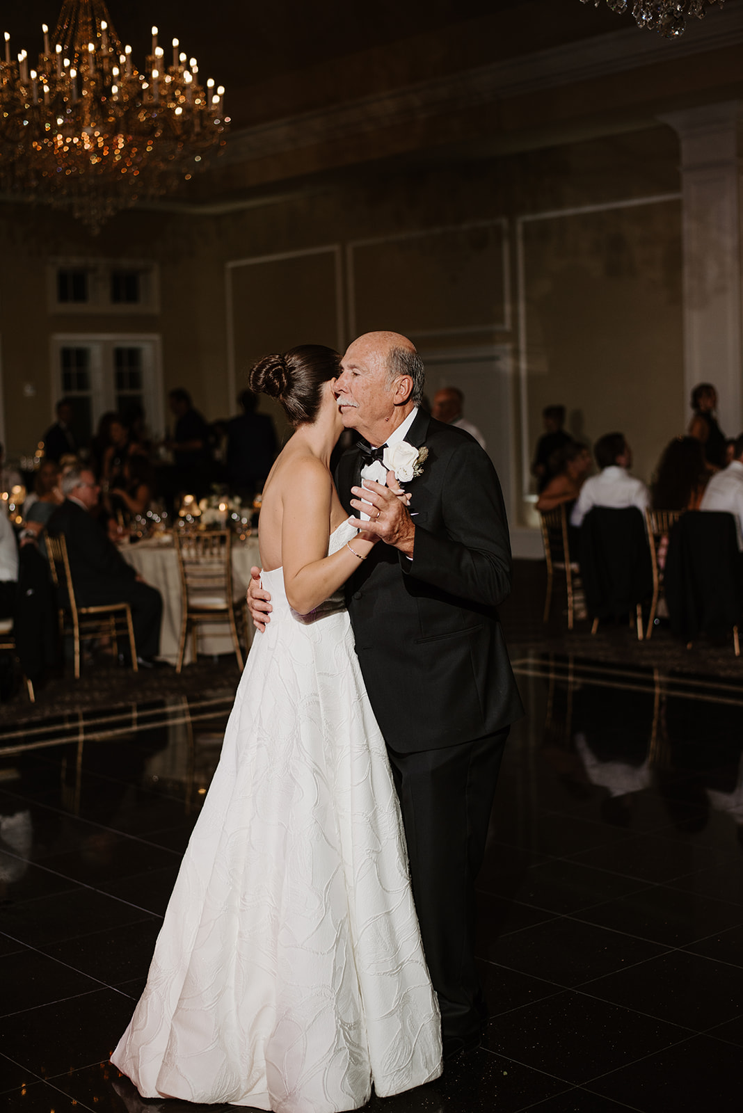Father kissing the bride's cheek in a sweet, tender father-daughter dance on the black ballroom floor.